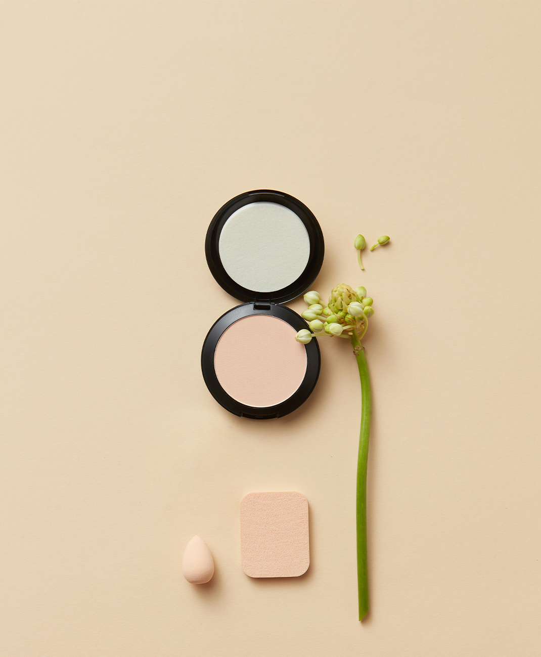 Compact powder with mirror, blush, and a flower on a beige background
